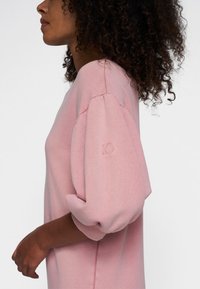Roze sweatshirt met een ontspannen pasvorm, voorzien van pofmouwen en ribgebreide manchetten. Kleine reliëfdetails tonen het nummer "10" op de mouw.