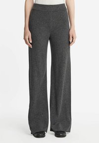 Antracietgrijze, wijde broek gemaakt van een zachte gebreide stof. Heeft een naadloze tailleband en licht uitlopende pijpen, gecombineerd met zwarte schoenen.
