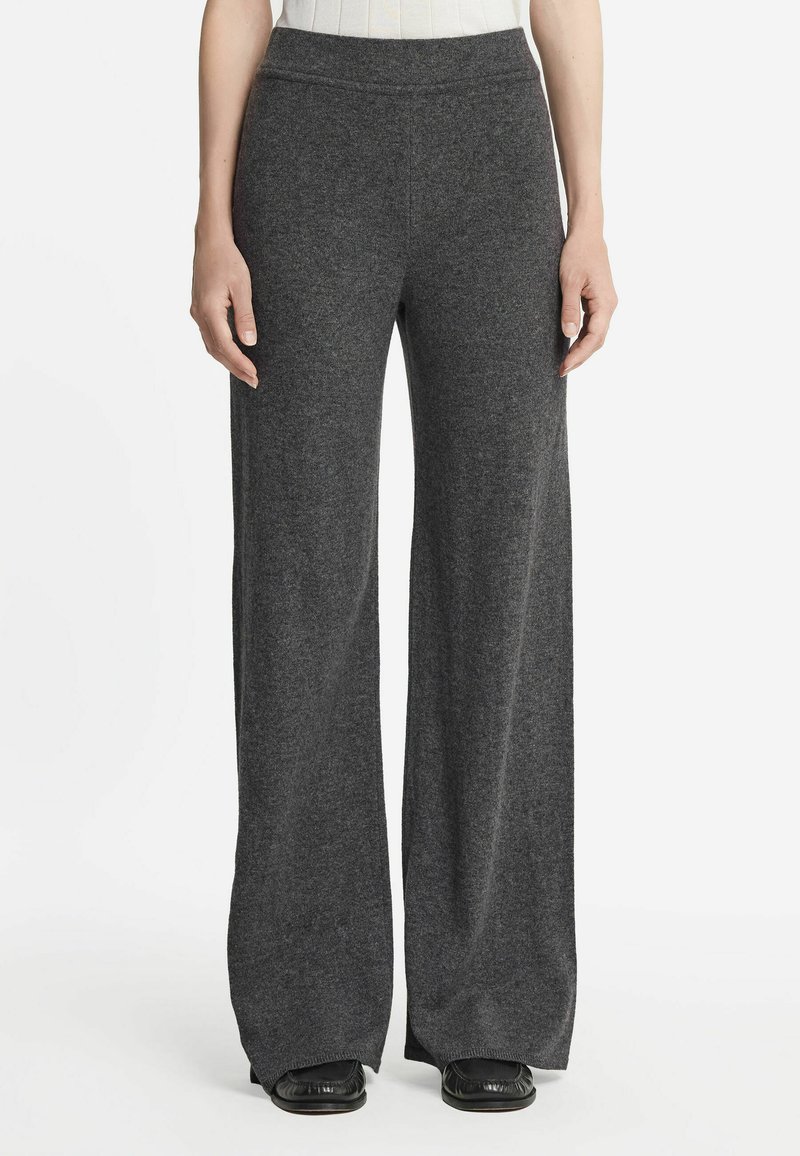 Antracietgrijze, wijde broek gemaakt van een zachte gebreide stof. Heeft een naadloze tailleband en licht uitlopende pijpen, gecombineerd met zwarte schoenen.