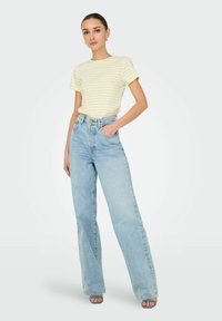 Stribet gul kortærmet skjorte og lyseblå højtaljede brede jeans med fem lommer. Enkel stofstruktur og minimale detaljer.