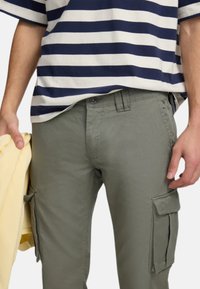 Pantalones cargo verde oliva con bolsillos laterales, combinados con una camiseta a rayas azul marino y blanca. La textura parece suave, la tela es ligera.