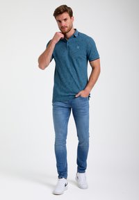 Polo teal avec un motif subtil, à manches courtes et col. Associé à un jean slim-fit bleu clair et des baskets blanches.