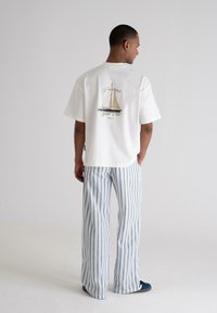 White cotton t-shirt with a sailboat graphic on the back, paired with blue and white striped wide-leg trousers. Smooth texture and relaxed fit.