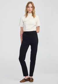 Crème kortemouwen top, zwarte op maat gemaakte broek en schoenen met panterprint. Glad materiaal, aangesloten ontwerp en minimale details.