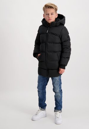 Zwarte pufferjas met een capuchon, voorzien van horizontale stiksels, ritsluiting en geribbelde manchetten, gecombineerd met blauwe jeans en witte sneakers.