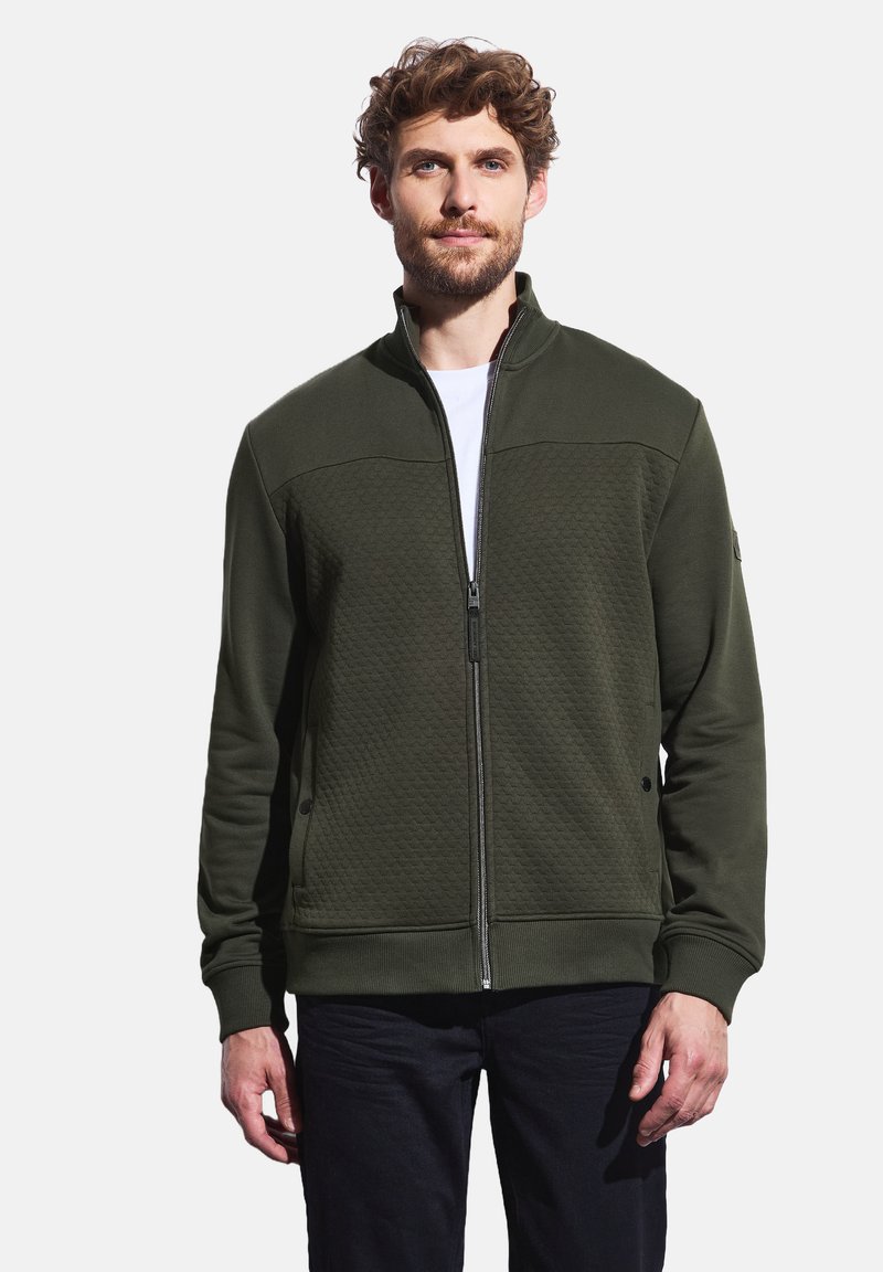 Veste zippée verte avec un panneau supérieur texturé, des poignets côtelés et des poches latérales. Fabriquée en tissu doux, elle affiche une coupe moderne.