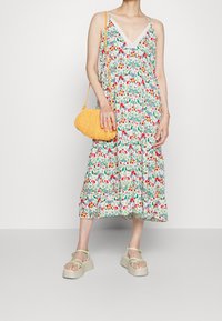 Abito floreale con spalline sottili, dettaglio in pizzo e orlo svasato. Borsa intrecciata gialla con forma curva. Sandali verde chiaro con suola piattaforma.