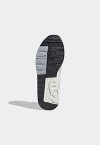 Svart, grå och vit sneakersula med texturerad gummi, med ett mönstrat grepp och en inbäddad logotyp i en upphöjd sektion.