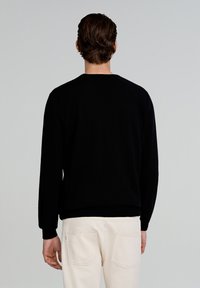 Suéter negro de punto con mangas largas y cuello redondo. Puños y dobladillo ajustados. Combinado con pantalones beige claros, de textura suave y sin patrones visibles.
