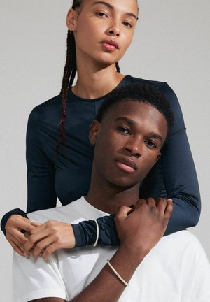 Navy long-sleeve top and white T-shirt, with one person embracing the other. Notable accessories include thin bracelets on both wrists.