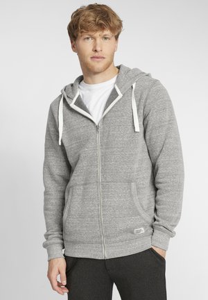 Gray zip-up hoodie with a white drawstring, kangaroo pockets, ribbed cuffs, and a fabric label at the hem, paired with a white t-shirt underneath.