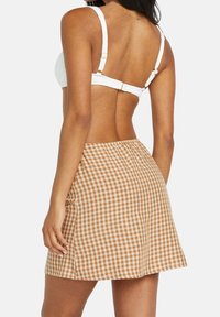 Falda corta de cuadros en tejido de cuadros marrón y blanco con cintura ajustada y ligera campana. Fabricada en un tejido ligero con una textura suave.