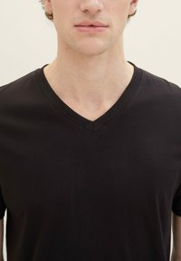 Zwart T-shirt met V-hals, gemaakt van zacht katoen. Heeft een subtiele textuur, korte mouwen en een klassieke pasvorm. Minimalistisch ontwerp zonder afbeeldingen.