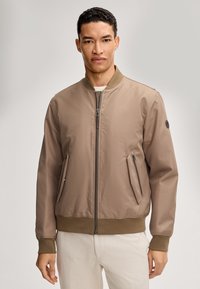 Giacca bomber marrone chiaro realizzata in tessuto liscio, con zip frontale, due tasche laterali e polsini e orlo a coste.
