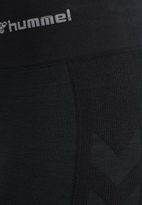 Zwarte sportlegging met een textuurstof, strepen en een logo op de tailleband. Het ontwerp heeft een chevronpatroon aan de zijkant.
