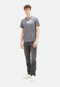 Gray short-sleeve t-shirt with a beach scene graphic featuring a sun and waves. Paired with dark jeans and white sneakers.