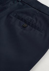 Tissu bleu marine avec un gros plan sur une poche arrière dotée d'une fermeture à bouton et de coutures visibles.