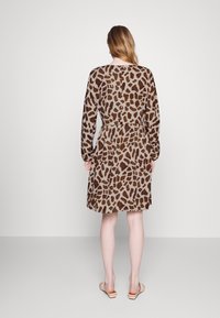 Brown animal print dress in a soft fabric. Long sleeves, belted waist, knee-length, and rounded hem. Worn with light-colored sandals.