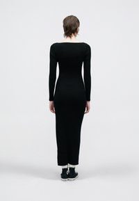 Rochie neagră cu mâneci lungi, cu dungi, decolteu pătrat, siluetă ajustată și tiv până la glezne. Purtați cu adidași negri și șosete albe.