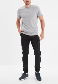 Graues Kurzarm-T-Shirt, schwarze Cargo-Hosen mit Seitentaschen und dunklen Sneakern. Einfaches Design mit lässiger Passform und glatter Textur.