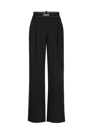 Zwarte broek met wijde pijpen en een elastische tailleband met de tekst "19V69" in het wit middenvoor.