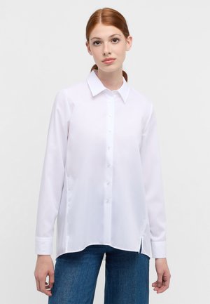 Camicia bianca a maniche lunghe con colletto tradizionale, abbottonatura frontale completa e spacchi laterali. Il tessuto appare liscio e leggermente lucido.