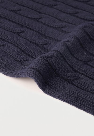 Tissu tricoté bleu foncé avec un motif côtelé et torsadé, plié sur une surface blanche.