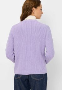 Lila Strickpullover mit Rippstruktur, langen Ärmeln und rundem Ausschnitt, kombiniert mit dunkelblauen Jeans, von hinten betrachtet.