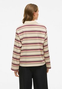 Lange mouw gestreepte top in beige met donkerrode en roze lijnen. Heeft een ontspannen pasvorm en een rechte zoom. Gemaakt van zacht katoen.