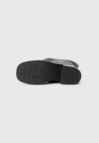 Bota de cuero negro con un upper suave y una suela de goma texturizada con marca en relieve. El diseño es elegante y aerodinámico.