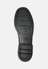 Svart gummisul med texturerad yta, räfflade kanter och ingraverade märkesdetaljer. Har cirkulära mönster för grepp och spår.