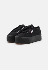 Sorte lerret sneakers med tykk gummisåle, rund tå og snøring. Har metalløye og et logo-patch på siden.