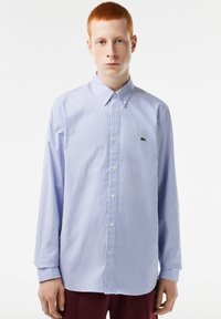 Camisa de manga larga, con botones, en rayas celestes y blancas. Presenta un cuello clásico y un pequeño logo verde en el pecho. Fabricada en algodón.