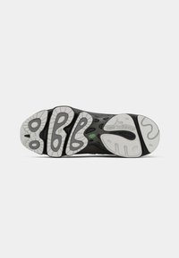 Semelle d’une chaussure New Balance noire et grise avec des motifs antidérapants texturés et le logo visible sur un fond blanc uni.
