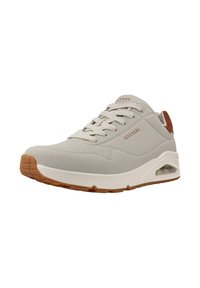 Zapatilla deportiva gris claro con un upper suave, acentos perforados, suela acolchada color beige y detalles de suela de goma marrón.