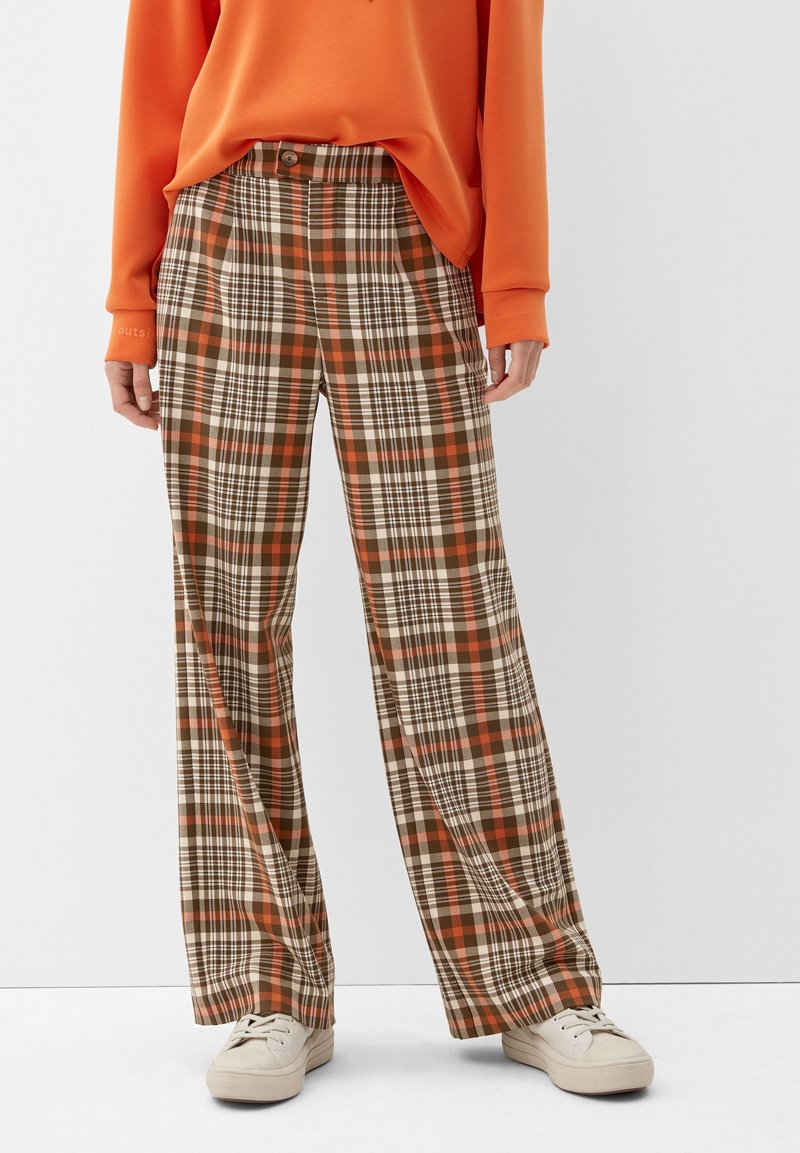 Geruite broek in bruin, oranje en crème. Heeft een hoge taille, wijde pijpen, knoopsluiting en subtiele textuur. Gepaard met lichte sneakers.