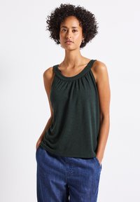 Haut sans manches vert foncé avec un décolleté arrondi, tissu froncé à l'avant et texture lisse. Associé à un pantalon bleu ample.