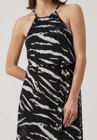 Czarna i biała w paski sukienka na ramiączkach z wiązanym paskiem w talii. Wykonana z lekkiego materiału, ma zgromadzony dekolt i luźny fason.