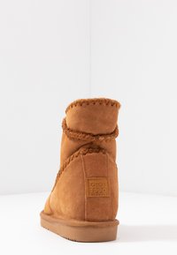 Botte en suède tan à la cheville avec détail cousu autour du col et semelle en caoutchouc. Comprend un patch de la marque à l'arrière.