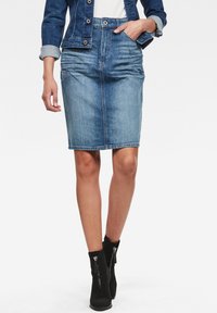 Jupe crayon en denim bleu clair avec une coupe droite, cinq poches et passants de ceinture, associée à des bottines noires à glissière.