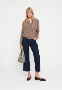 Cardigan texturat maro cu nasturi, cămașă albă, blugi scurți de culoare bleumarin și loafers burgundy. Ținând o geantă cu model de piele de șarpe.