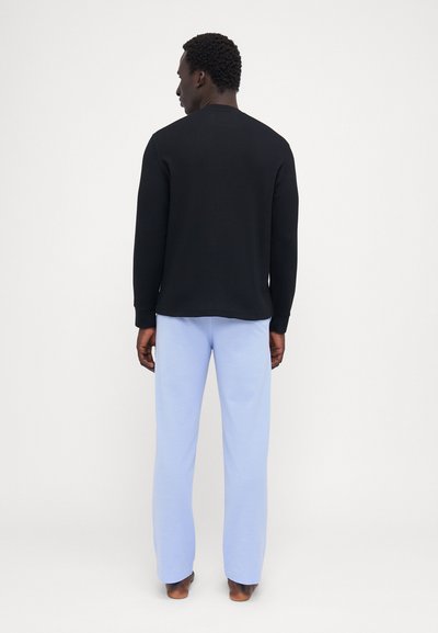 Camisa preta de mangas longas combinada com calças largas de tom azul claro. A camisa tem um decote redondo e textura canelada, enquanto as calças são lisas.