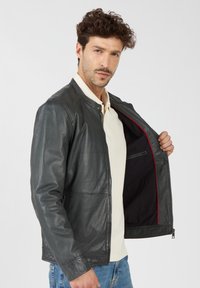 Grijze leren jas met een klassieke kraag, ritsluiting en rode voering. Beschikt over een gladde textuur en minimale hardware-accenten.