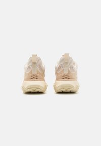 Beige Sport Schuhe mit einer strukturierten Mesh-Oberfläche, verstärktem Fersenbereich und einer dicken, gemusterten Gummisohle sowie einer Ziehschlaufe auf der Rückseite.