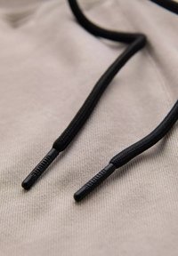 Tissu beige clair avec des cordons texturés noirs dotés d'embouts en plastique noir. Les cordons sont soigneusement disposés sur la surface.