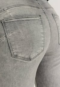 Zbliżenie na szare dżinsy z widocznym przeszyciem i tylnymi kieszeniami, noszone przez osobę.