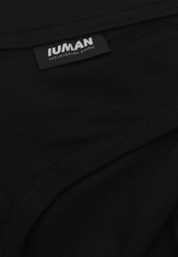 Svart tygtröja med sydd fåll, med en framträdande vit etikett som säger "IUMAN" och "intimissimi uomo." Mjuk, slät textur.