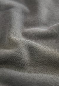 Gros plan sur un tissu tricoté doux, gris, avec une texture fine visible et des plis doux créant des vagues ombrées.