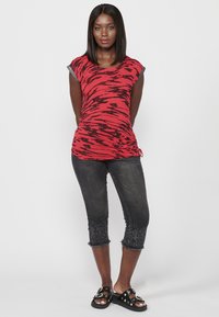 Haut rayé rouge et noir à manches courtes, associé à des capris en denim foncé avec des ourlets décorés et des sandales à glissière noires.