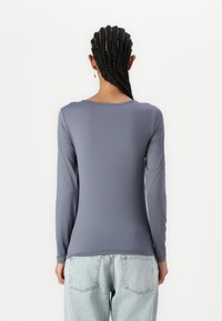 Long-sleeve, light gray shirt with a rounded neckline, smooth texture, and a fitted design. Paired with high-waisted light blue jeans.